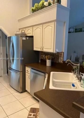 Kitchen area featuring white cabinetry, dark solid-surface countertops, stainless steel appliances, ceramic tile flooring, and a double-basin sink with a gooseneck faucet