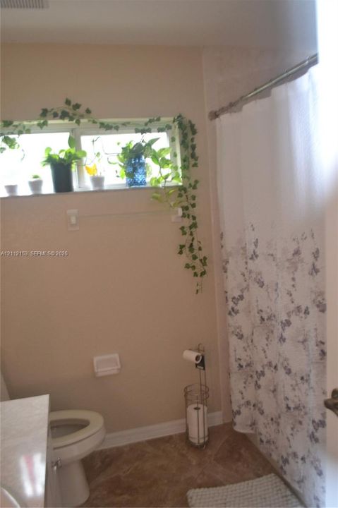 Bathroom featuring a horizontal window with stone sill, ceramic tile flooring, and a metal shower rod