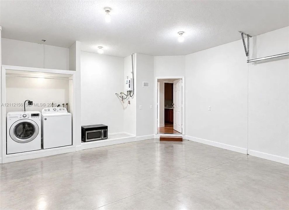 Finished interior space featuring smooth concrete flooring, white walls, and built-in laundry hookups with an overhead light fixture and wall-mounted tankless water heater