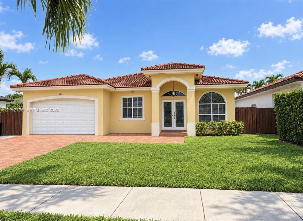 Stucco exterior with a tiled roof, arched entryway, brick-paver driveway, and a multi-paned arched window