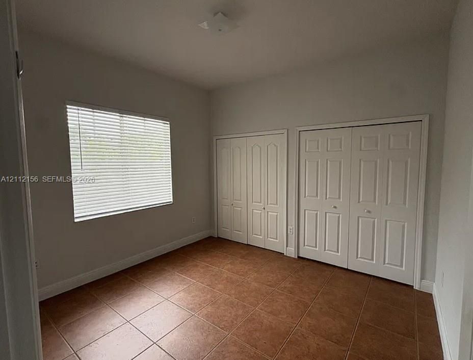 Room featuring neutral wall paint, tile flooring, two white panel-door closets, and a window with horizontal blinds