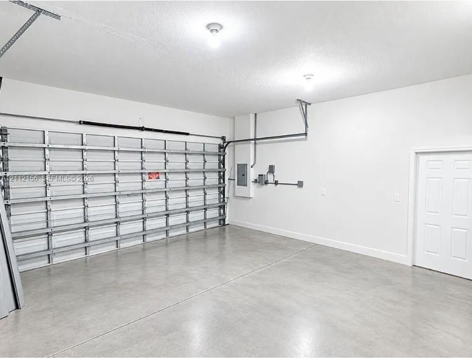 Finished garage interior featuring a smooth-finish concrete floor, high-ceiling structure, white-painted walls, and a multi-panel steel garage door