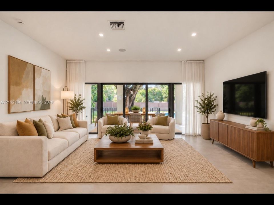 (Digitally staged) Bright living area with large-format tile, recessed lighting, and multi-panel sliding glass doors that open to the covered patio for seamless indoor-outdoor living