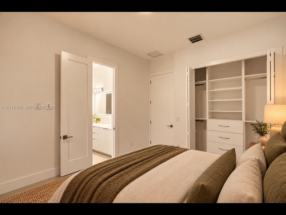 (Digitally staged) Comfortable bedroom with neutral walls, and a closet with built-in shelving and drawers