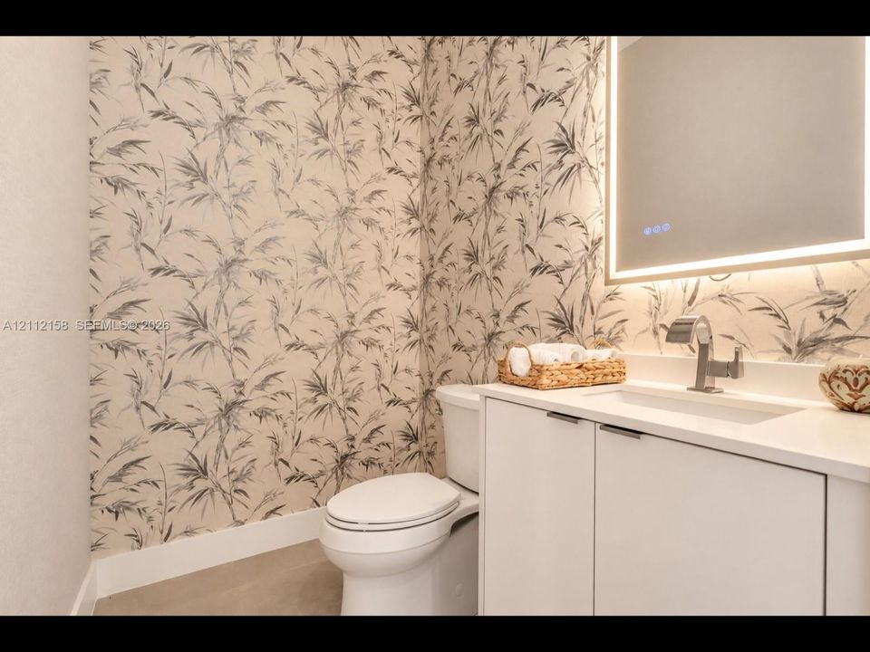 Stylish bathroom with designer patterned wallpaper, white vanity, chrome fixtures, and a modern LED-backlit mirror