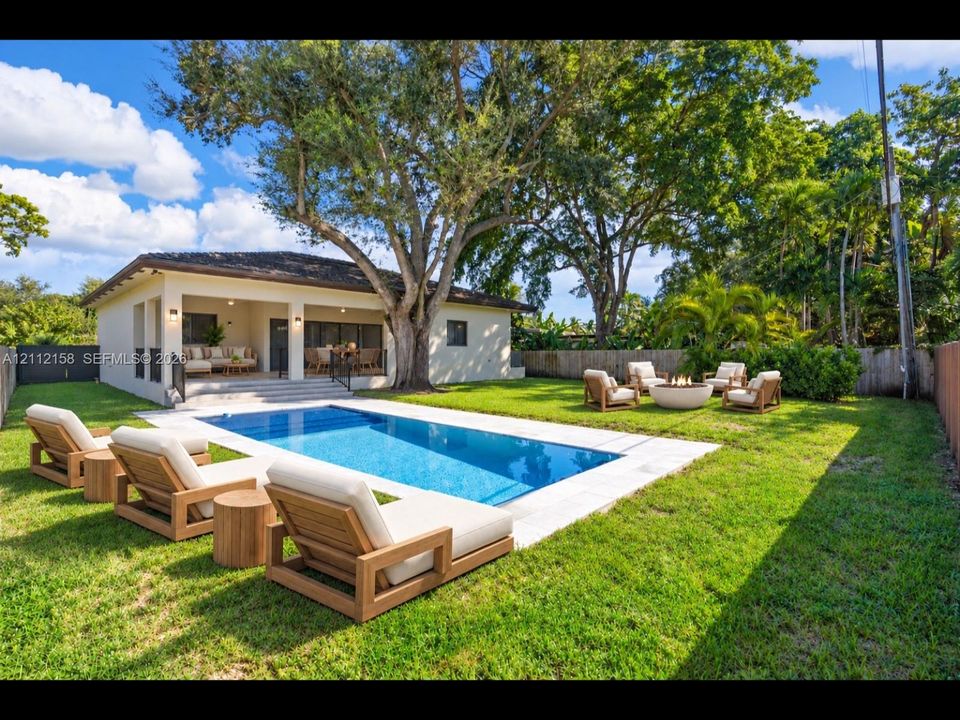 (Digitally staged) Resort-style backyard with an in-ground pool, stone paver deck, covered patio, and mature trees for natural shade and privacy