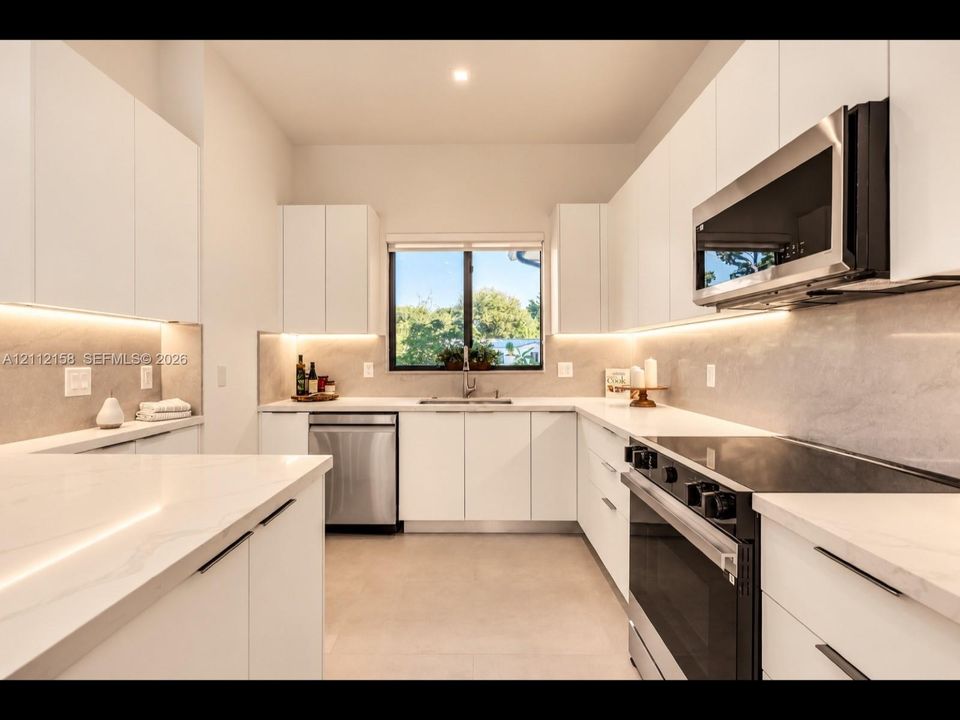 Modern kitchen with crisp white cabinetry, stone countertops, full-height stone backsplash, under-cabinet lighting, and stainless steel appliances