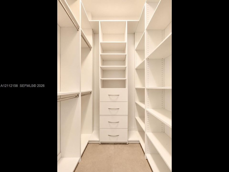 Organized walk-in closet with custom white built-ins, hanging rods, adjustable shelving, and a built-in four-drawer dresser