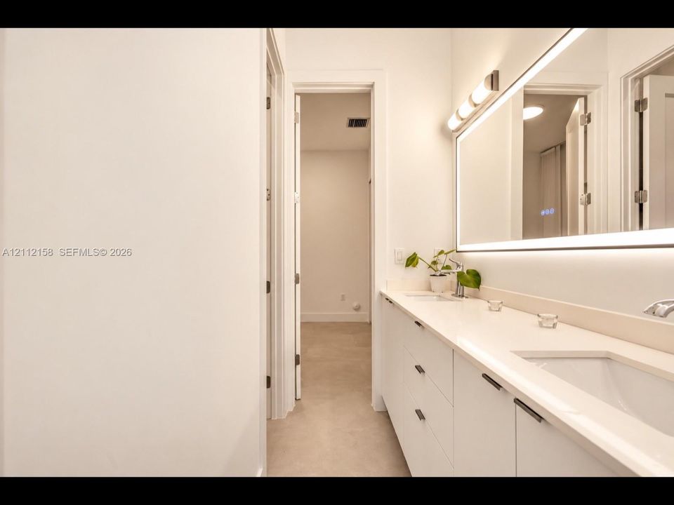 Elegant dual-sink vanity with stone countertop, sleek cabinetry, LED-backlit mirror, and brushed metal hardware