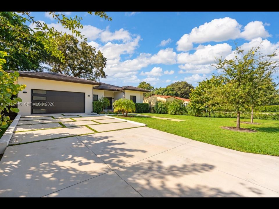 Inviting curb appeal with a modern garage door, tiered grass-inlay driveway, manicured lawn, and mature landscaping