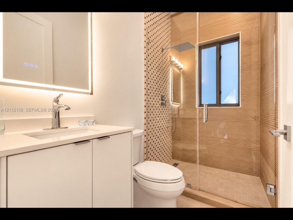 Spa-like bathroom with a frameless glass shower, rainfall showerhead, backlit mirror, and patterned tile accents