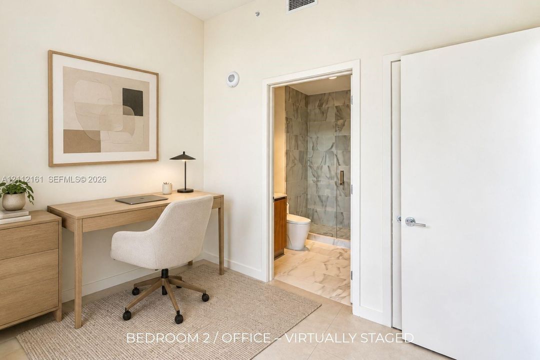 Neutral wall finishes with a full-height doorway opening to a bathroom featuring stone-patterned tile flooring, a glass-enclosed shower with large-format wall tile, and a wood-finish vanity cabinet
