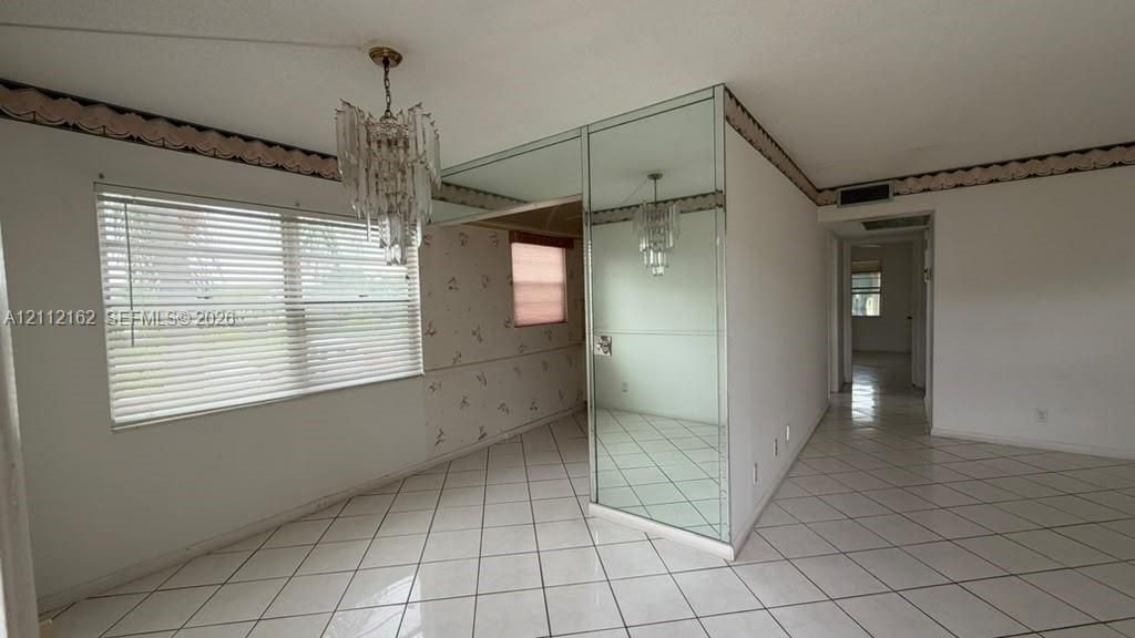 Interior space featuring white tile flooring, floor-to-ceiling mirrored wall cladding, and a multi-tiered crystal chandelier
