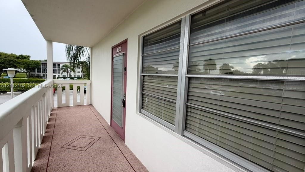 Covered exterior corridor with concrete flooring, white protective railing, and exterior entrance door