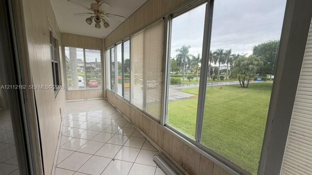 Enclosed sunroom featuring expansive glass windows, ceramic tile flooring, vertical wood-panel wall finish, and a ceiling-mounted light fixture