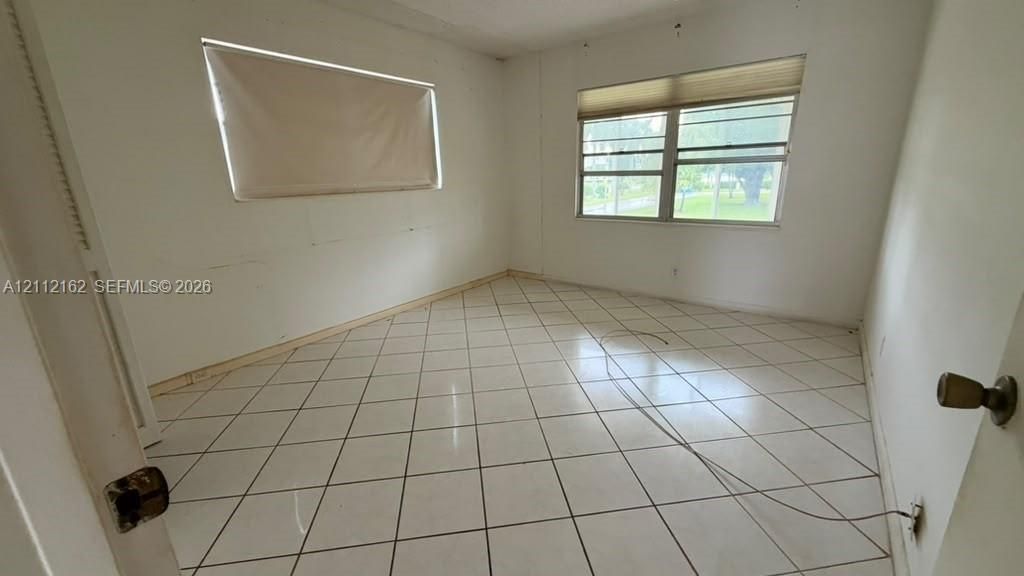 Bright room featuring neutral ceramic tile flooring and two windows with installed window treatments