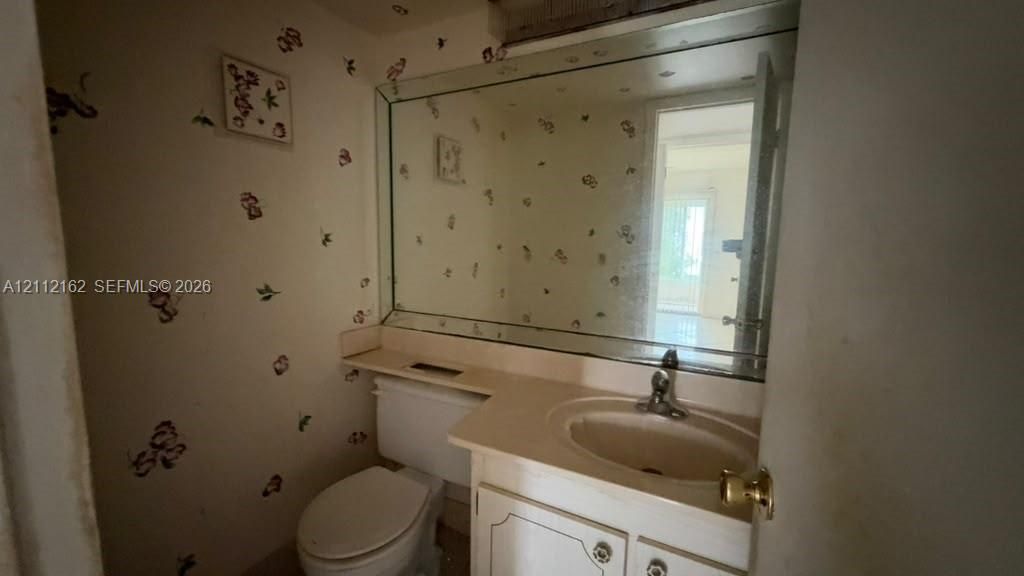 Vanity featuring a solid-surface countertop with an integrated basin, white cabinetry, a large wall-mounted mirror, and a porcelain toilet