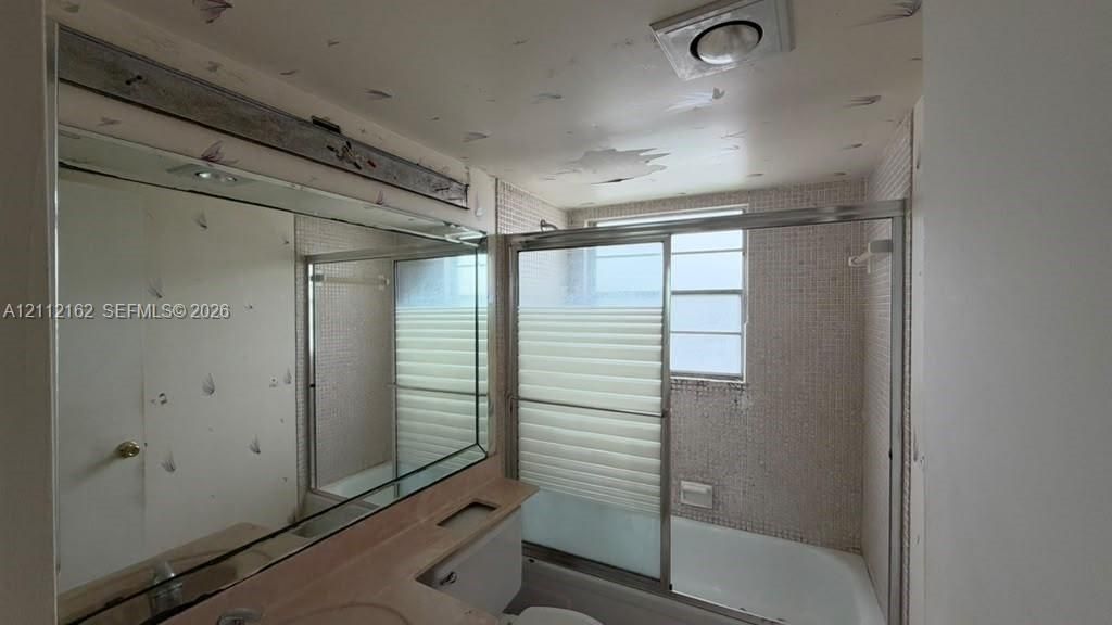 Full-width wall mirror, tub-shower combination featuring a sliding glass enclosure, and tiled surround
