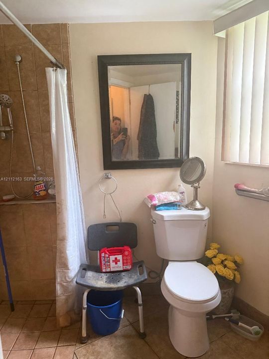 Tiled shower enclosure, wall-mounted mirror with a dark finish, and ceramic tile flooring