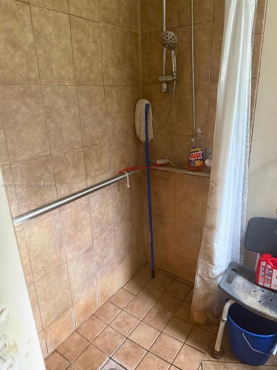 Walk-in shower enclosure featuring floor-to-ceiling tile, stainless steel grab bar, and wall-mounted shower fixture
