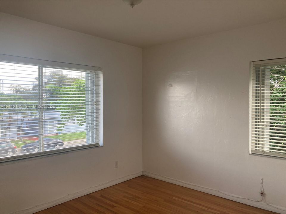 Interior space featuring wood-finish flooring, two windows with horizontal blinds, and a neutral wall finish