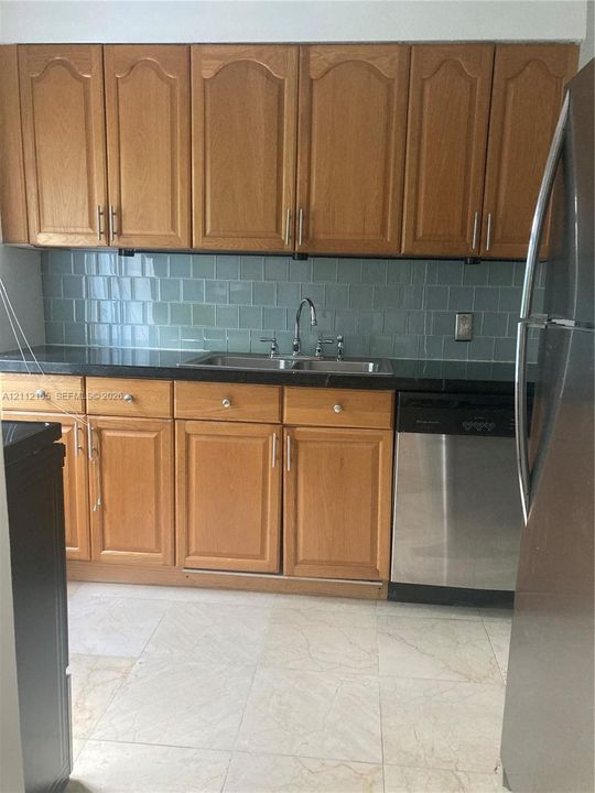 Kitchen featuring wood cabinetry, dark stone-finish countertops, stainless steel dishwasher, undermount dual-basin sink, and a light blue tile backsplash