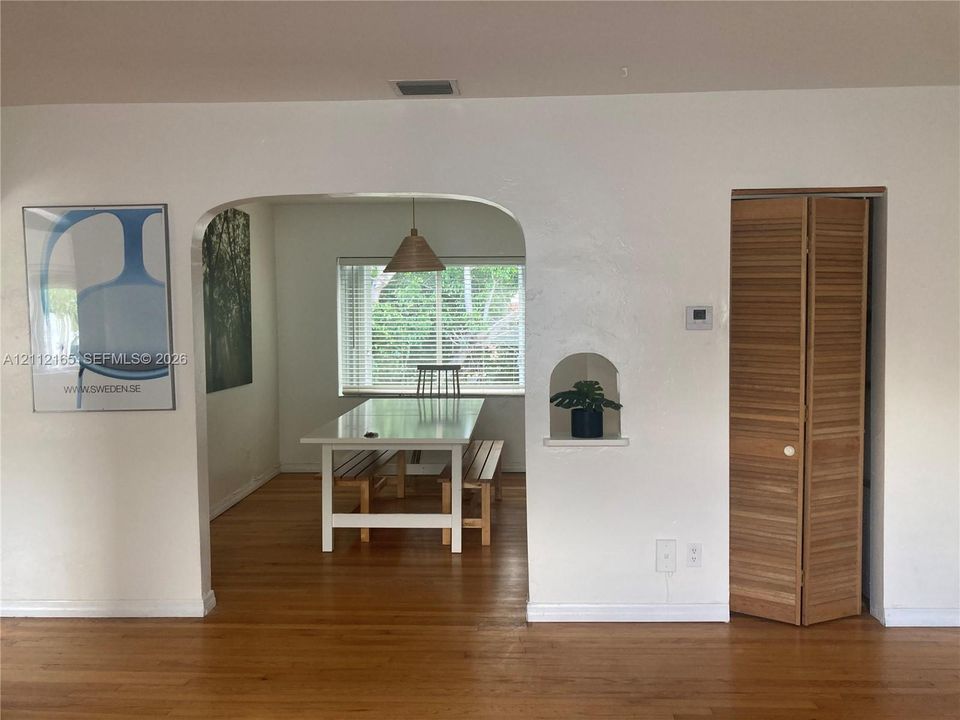 Interior space featuring wood-finish flooring, a prominent arched architectural opening, a built-in recessed wall niche, and natural-tone louvered bifold doors