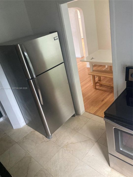 Stainless steel refrigerator, freestanding electric range with black cooktop, and neutral tile flooring