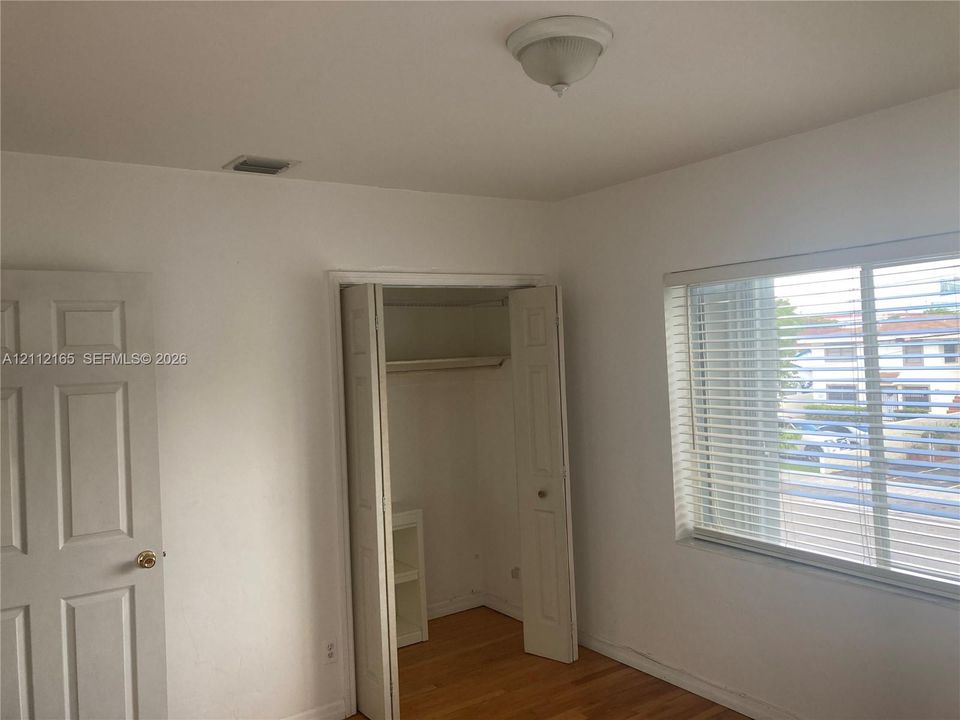 Room featuring wood-finish flooring, a bi-fold closet door, built-in shelving, and a multi-pane window with horizontal blinds