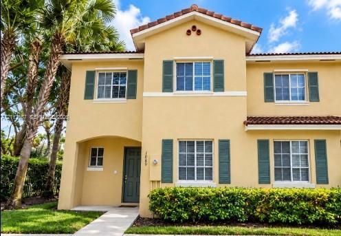 Stucco exterior featuring decorative shutters, a clay tile roof, and a paved entryway path