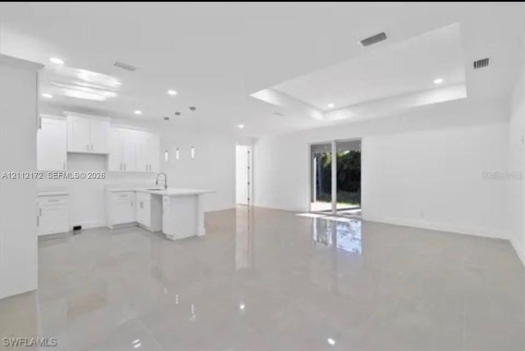 Open-concept floor plan featuring recessed lighting, a coffered ceiling, polished tile flooring, and a kitchen with white cabinetry and a center island