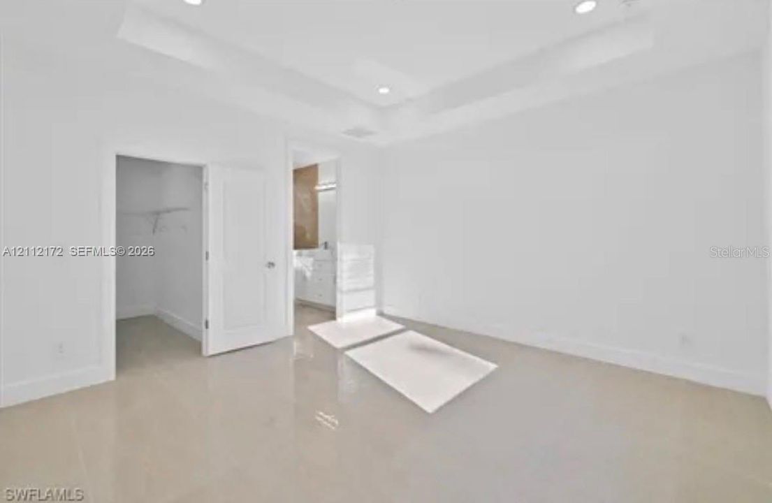 Tray ceiling with recessed lighting, large-format tile flooring, and walk-in closet featuring built-in wire shelving