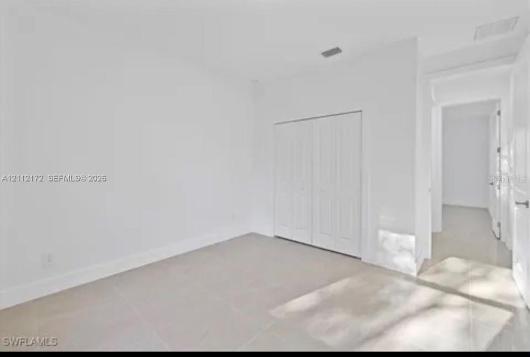 Neutral interior space featuring polished tile flooring, smooth white walls, and a built-in closet with dual paneled doors