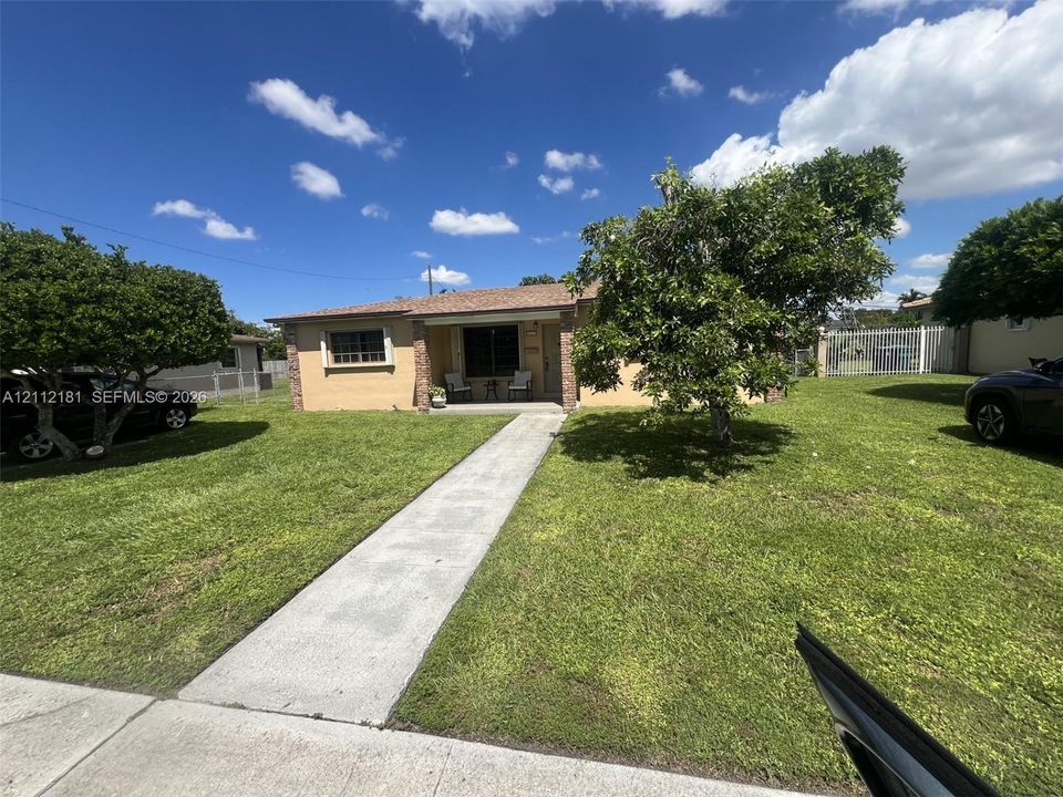 Stucco exterior with masonry-trimmed entry column, concrete walkway, and expansive front lawn featuring mature trees