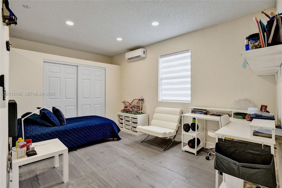 Room featuring wood-finish flooring, recessed lighting, sliding closet doors, a wall-mounted ductless air conditioning unit, and a window with horizontal blinds