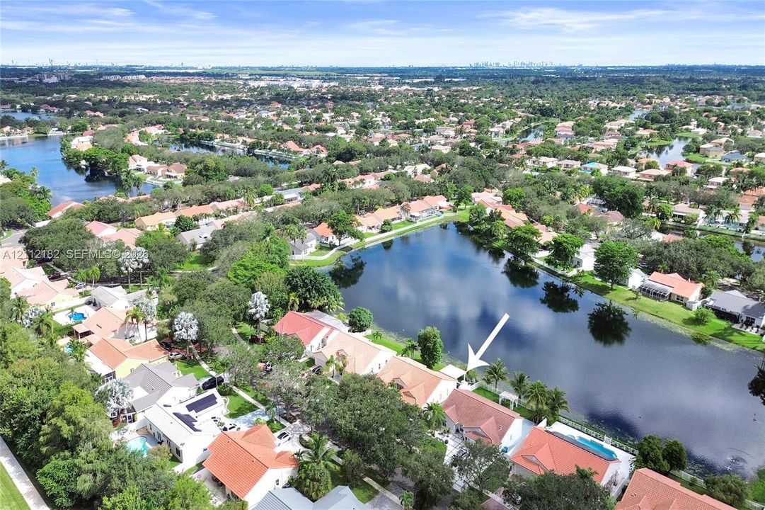 Aerial perspective of a waterfront property featuring a tile roof, paved driveway, and established landscaping