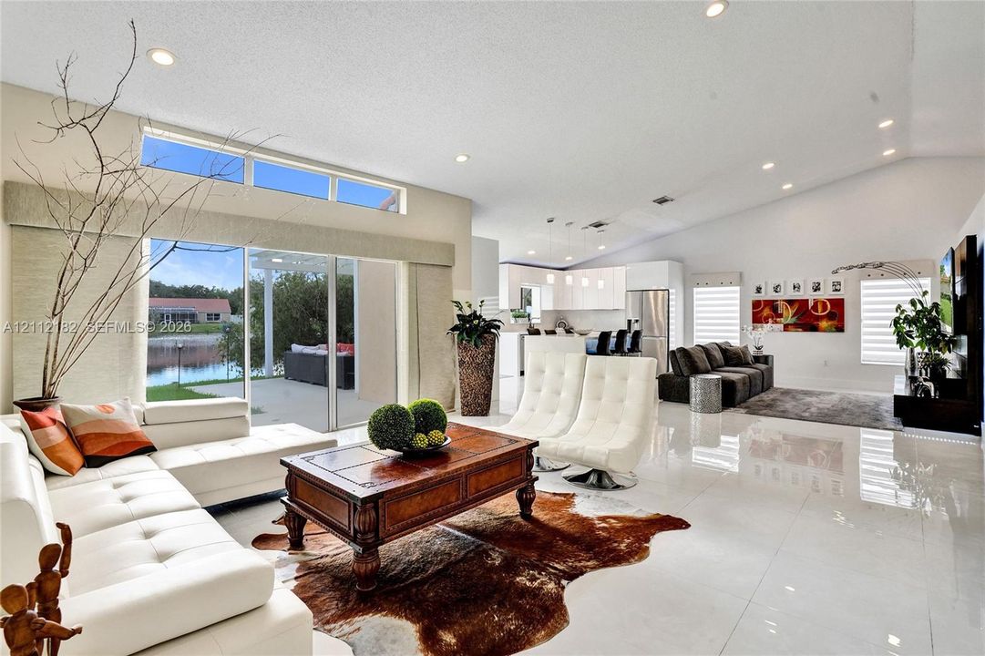Open-concept living area featuring vaulted ceilings, large-format tile flooring, recessed lighting, and expansive sliding glass doors with clerestory windows