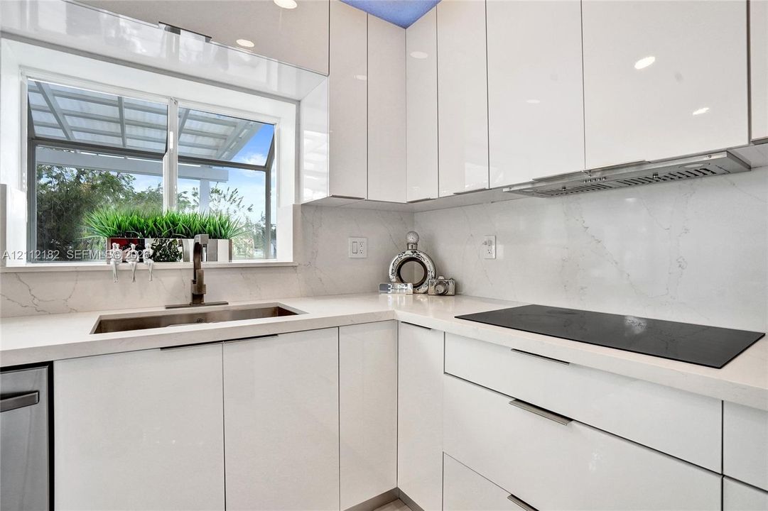 High-gloss white cabinetry, white stone-finish countertops, integrated stone-finish backsplash, undermount sink with gooseneck faucet, and built-in electric cooktop