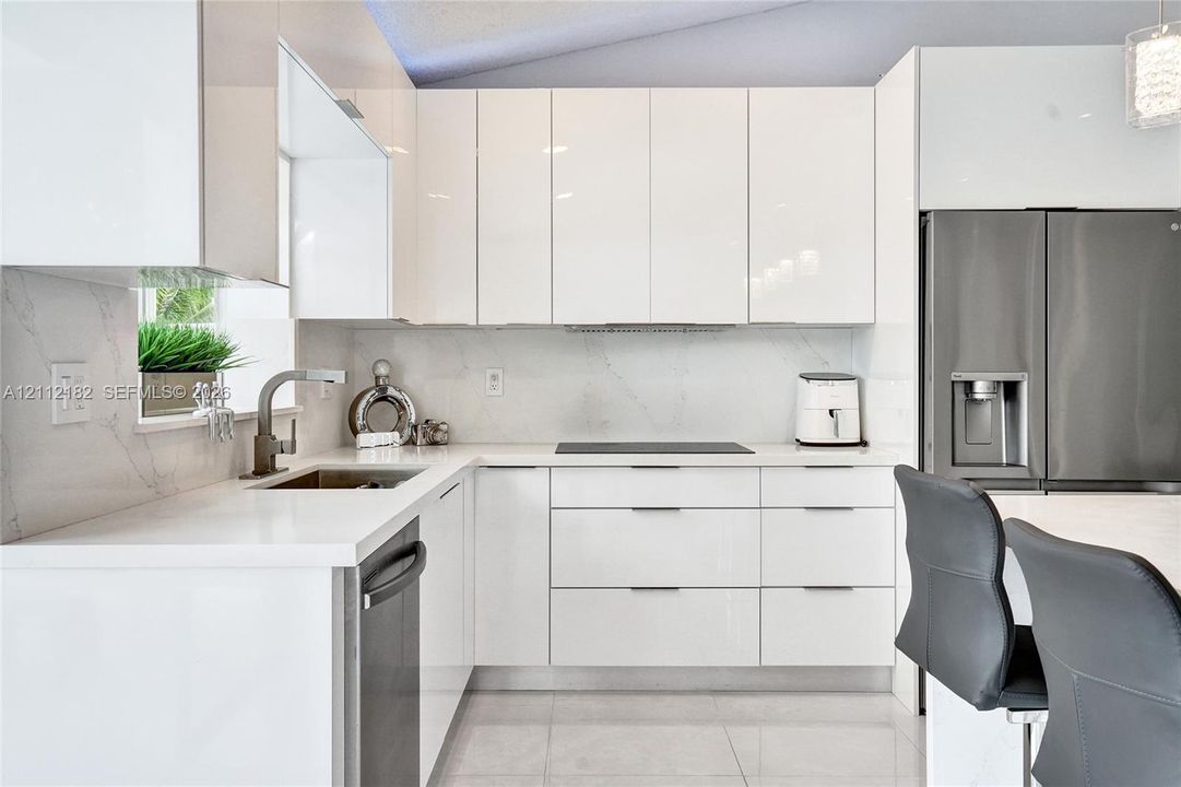 Modern kitchen featuring high-gloss cabinetry, stone-finish countertops, full-height backsplash, undermount sink with a gooseneck faucet, and integrated stainless steel appliances