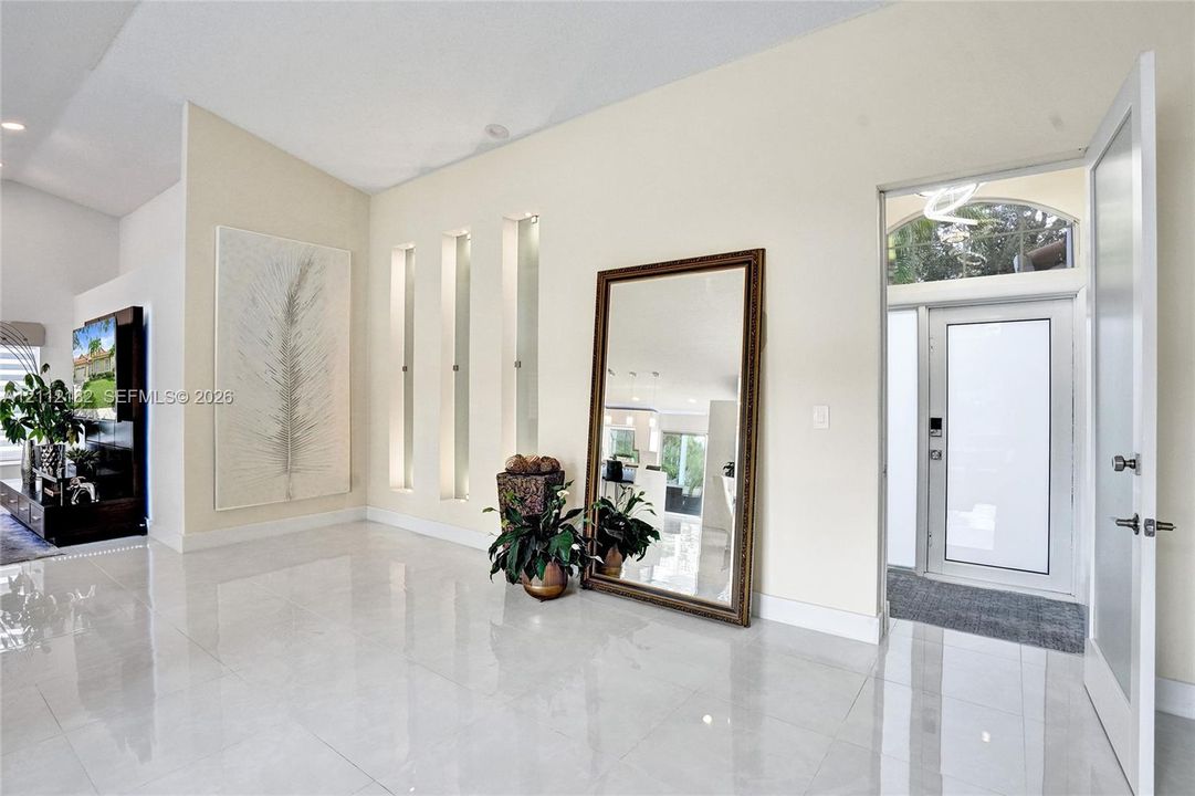 Entryway featuring large-format tile flooring, high vaulted ceilings, triple recessed wall niches, and a glass-paneled entry door with an arched transom window