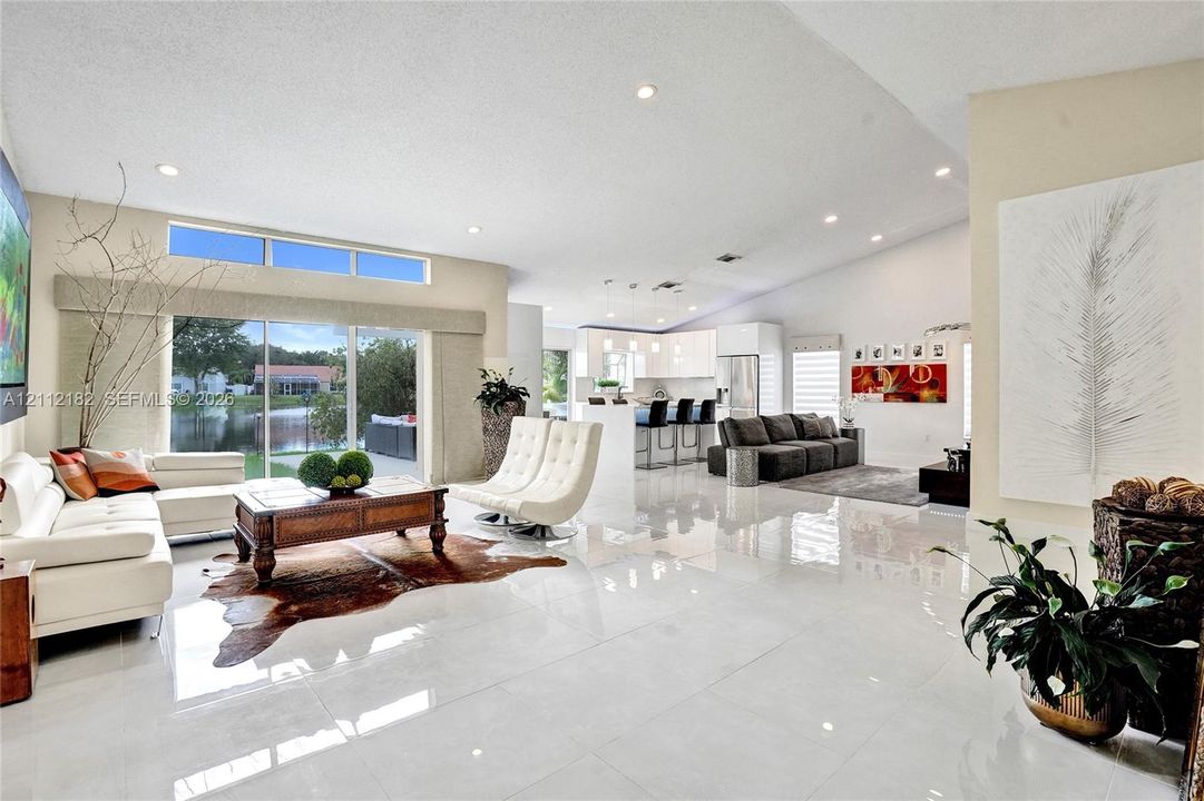 Open-concept interior featuring polished porcelain tile flooring, high vaulted ceilings, recessed lighting, expansive glass sliding doors, and transom windows