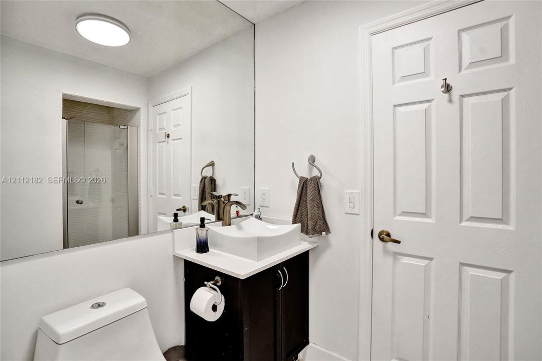 Vanity featuring a dark-finish base cabinet, solid-surface countertop, and white square vessel sink with a metallic faucet, complemented by a floor-to-ceiling mirror and a glass-enclosed shower