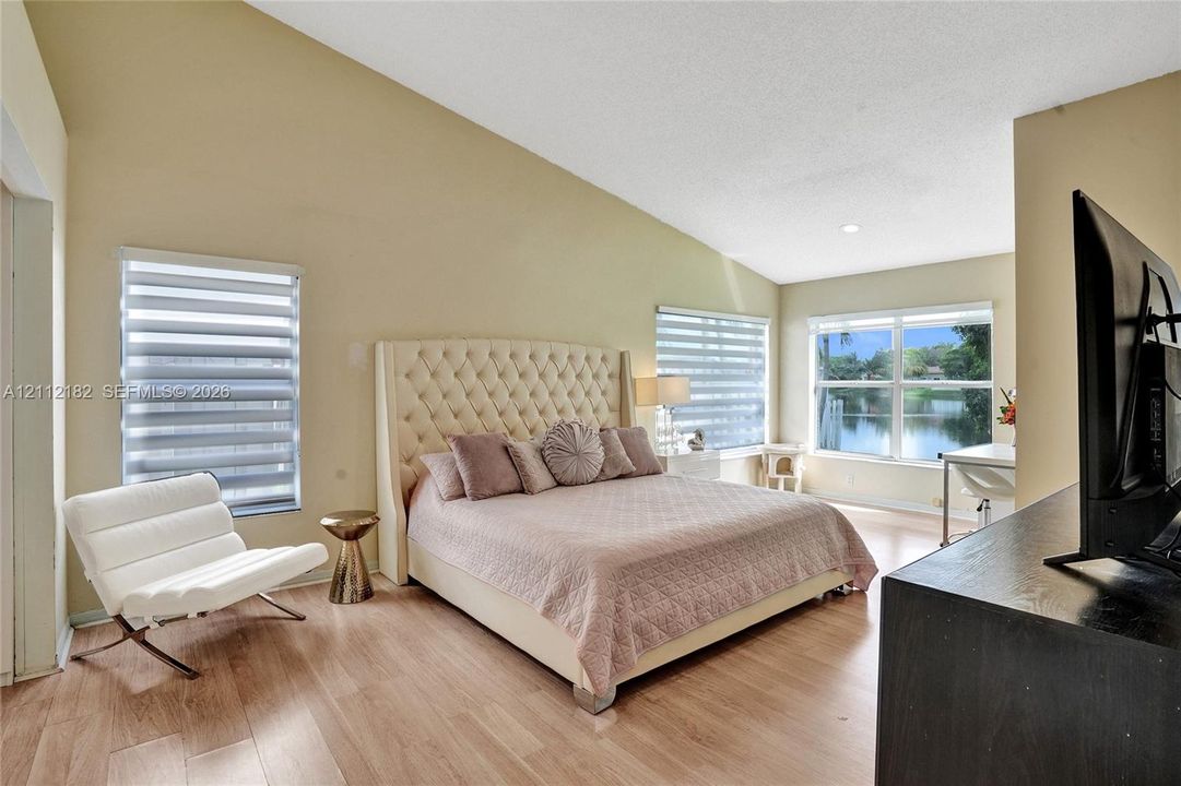 Vaulted ceilings, wood-finish flooring, dual-pane windows with horizontal blinds, and waterfront scenery