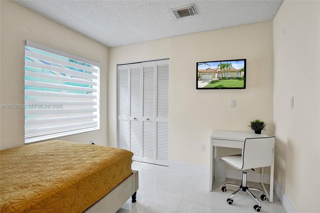 Neutral-toned interior featuring large-format tile flooring, louvered bi-fold closet doors, and adjustable window blinds