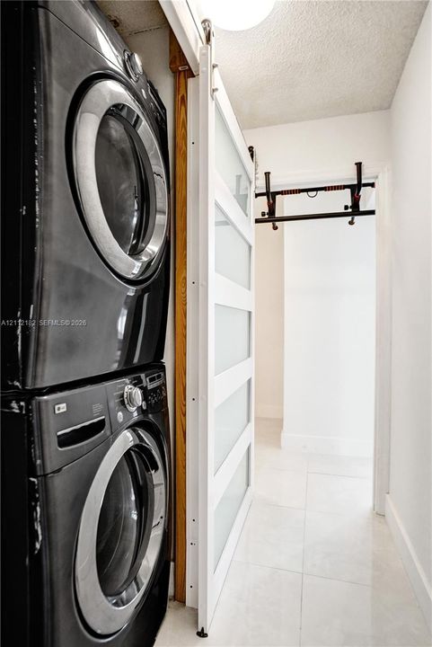 Stacked laundry units featuring a white sliding door with frosted glass panels and large-format tile flooring