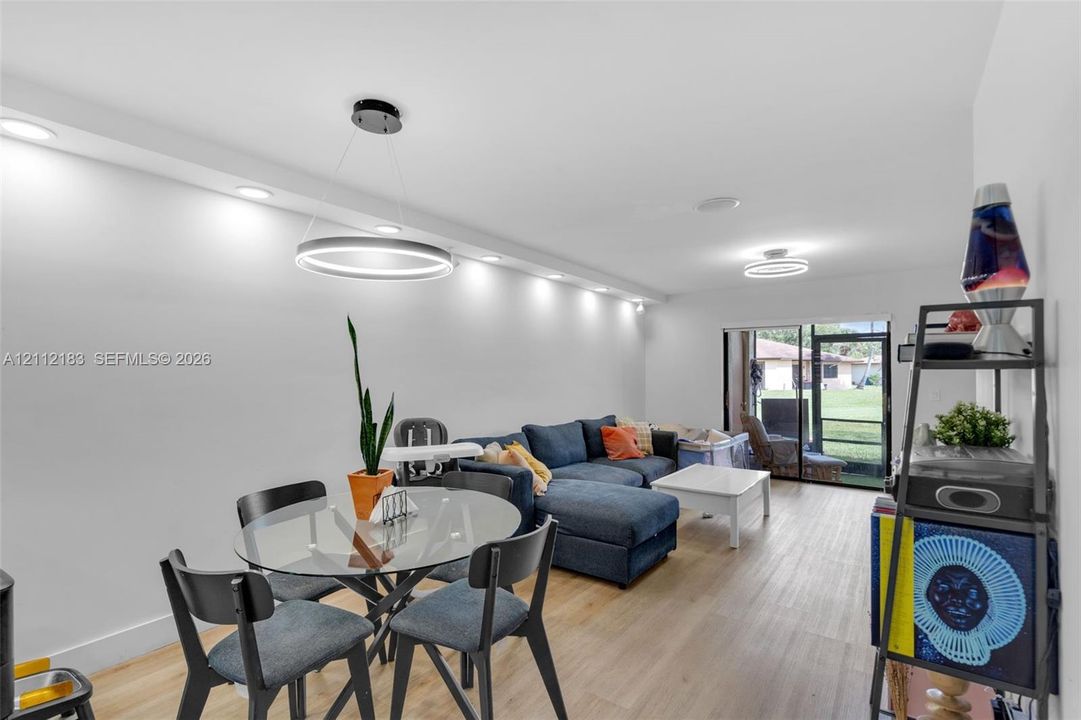 Open-concept living space featuring wood-finish flooring, recessed ceiling lighting, a modern circular LED pendant fixture, and sliding glass doors leading to an exterior area