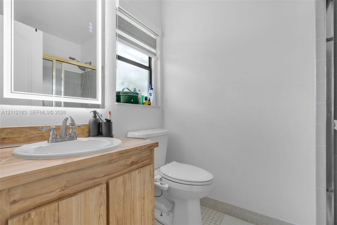 Wood-finish vanity with an integrated basin, metal faucet, illuminated mirror, and window with built-in blinds