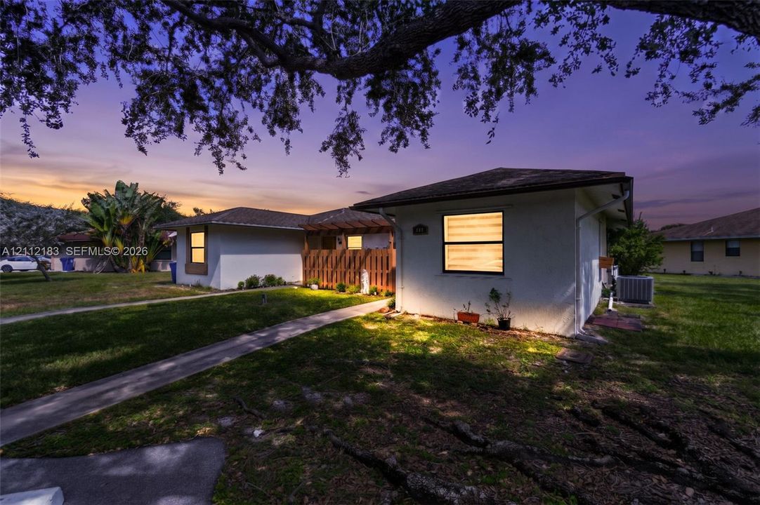 Single-story exterior featuring light-toned stucco siding, a low-pitched roof, horizontal sliding windows, and a wood-slatted privacy partition