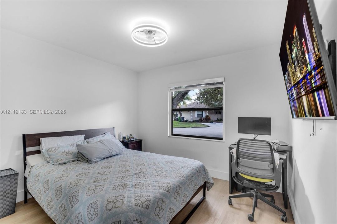 Bedroom featuring light-tone wood-finish flooring, a neutral color palette, a single-pane window with a horizontal blind, and a modern circular ceiling-mount light fixture