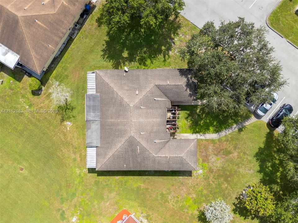 Aerial perspective featuring a hip roof, concrete walkway, mature trees, and open green space